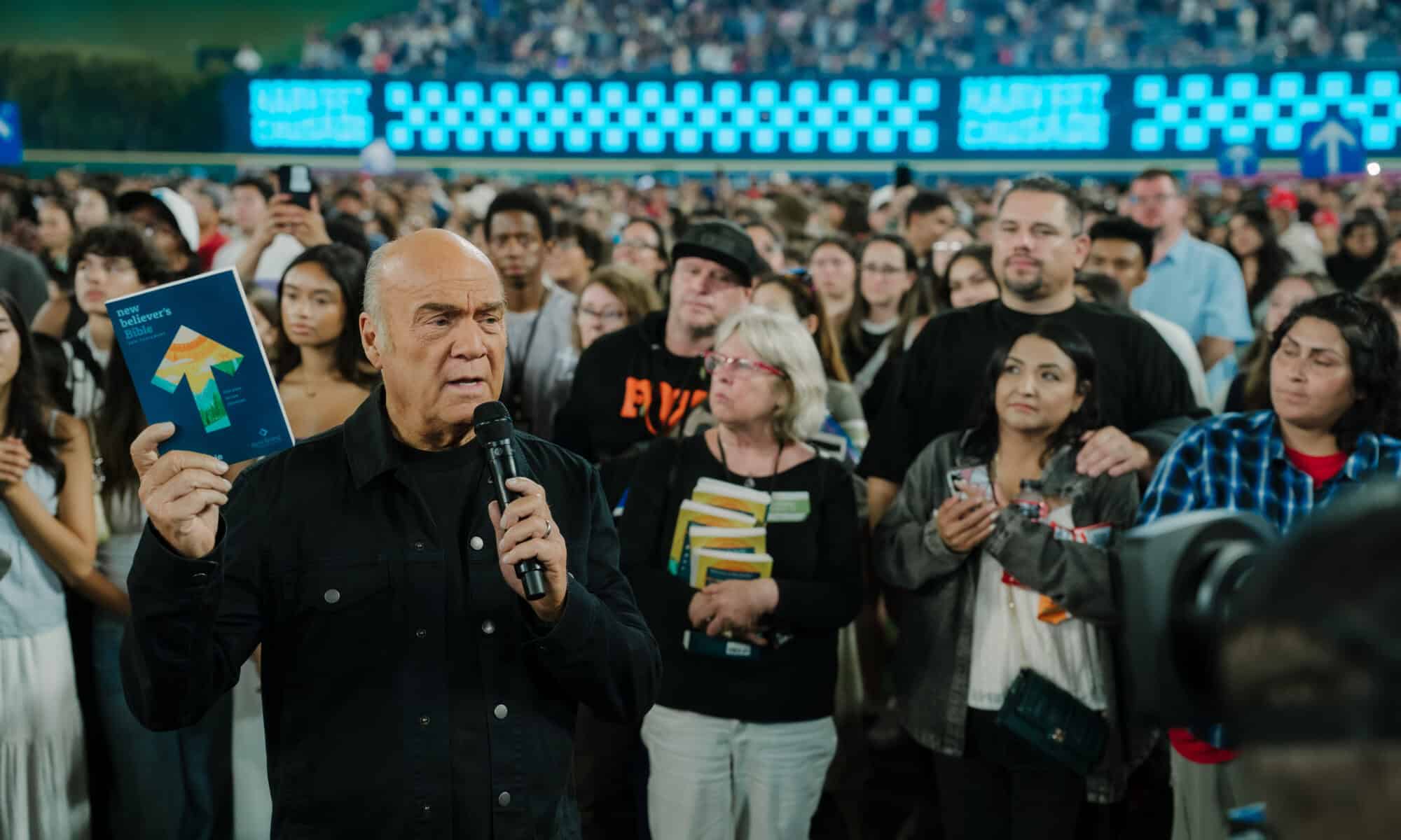 Greg Laurie holds up bible at 2025 harvest crusade with crowd